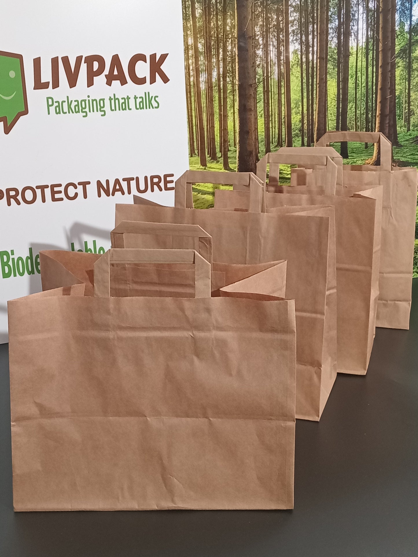 Sachets cabas kraft avec poignées plates Livpack sur fond bois et forêt